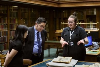 two people look at artefact as woman stands over