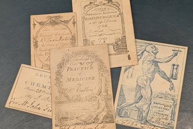 Five business card-sized class tickets from the University of Edinburgh. Each has the course title (chemistry, materia medica, anatomy) printed on it as well as handwritten names of the student attending. Some contain just text while others are more ornate with borders and even a copy of Andreas Vesalius’s image of a dissected man