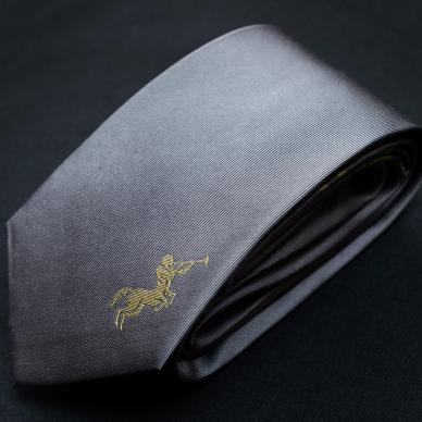 Photo of Grey silk tie with stitched gold Chiron emblem.